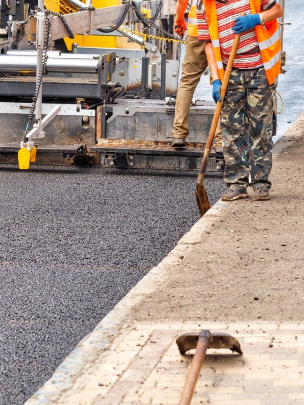 An industrial worker laying a layer of new hot asphalt on the carriageway
